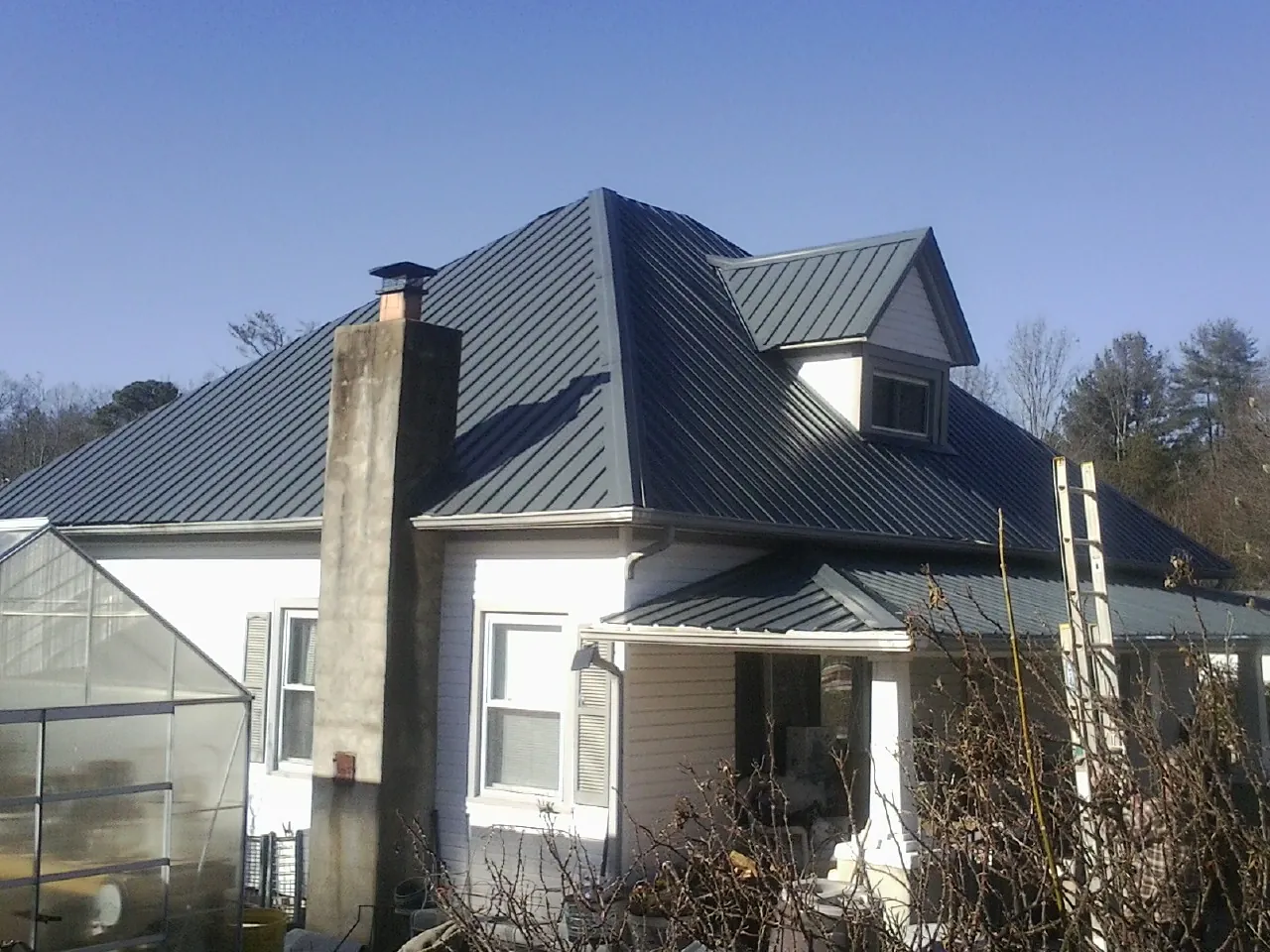Dark blue standing seam metal roof on a white farmhouse with dormer — Slate & Tile Roof Repair by Roofing Brothers in Wilbraham