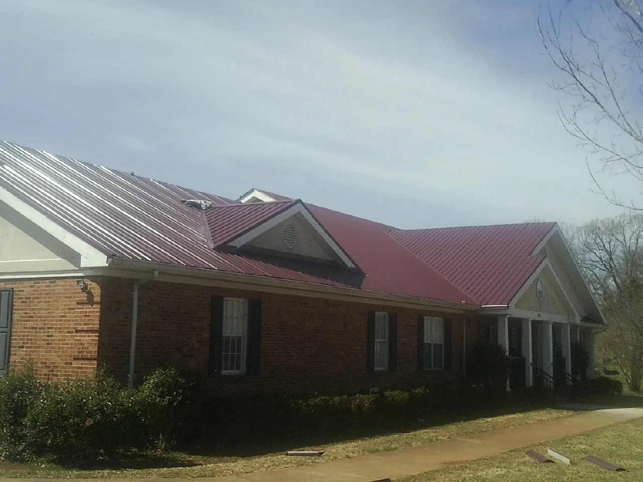 Red metal roof with gabled entries on a long brick building, from a Hail Damage Roof Repair job in Wilbraham
