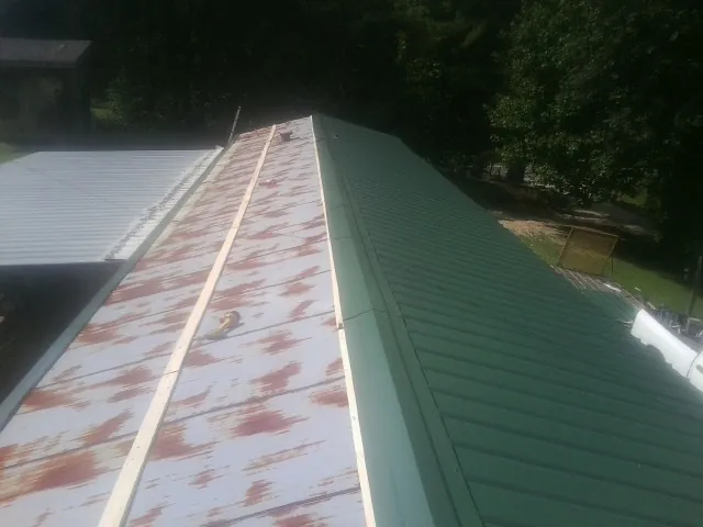 Old rusted panels beside newly installed green metal roofing — Wind Damage Roof Repair by Roofing Brothers in Wilbraham