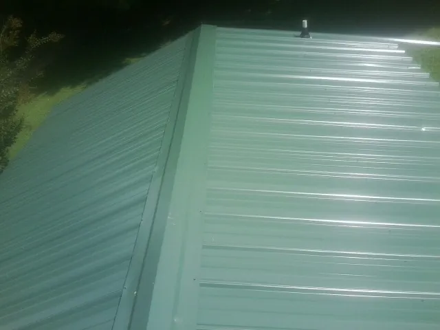 New green metal panels meeting at the ridge of a roof — Flat Roof Repair work by our crew in Wilbraham