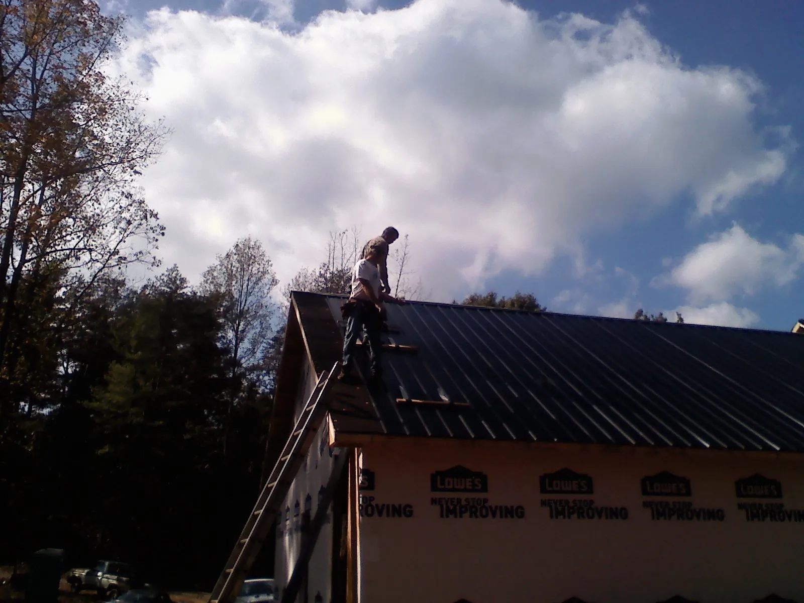 Roofer fastening dark metal panels high against a cloudy sky, from a Roof Inspection job in Wilbraham