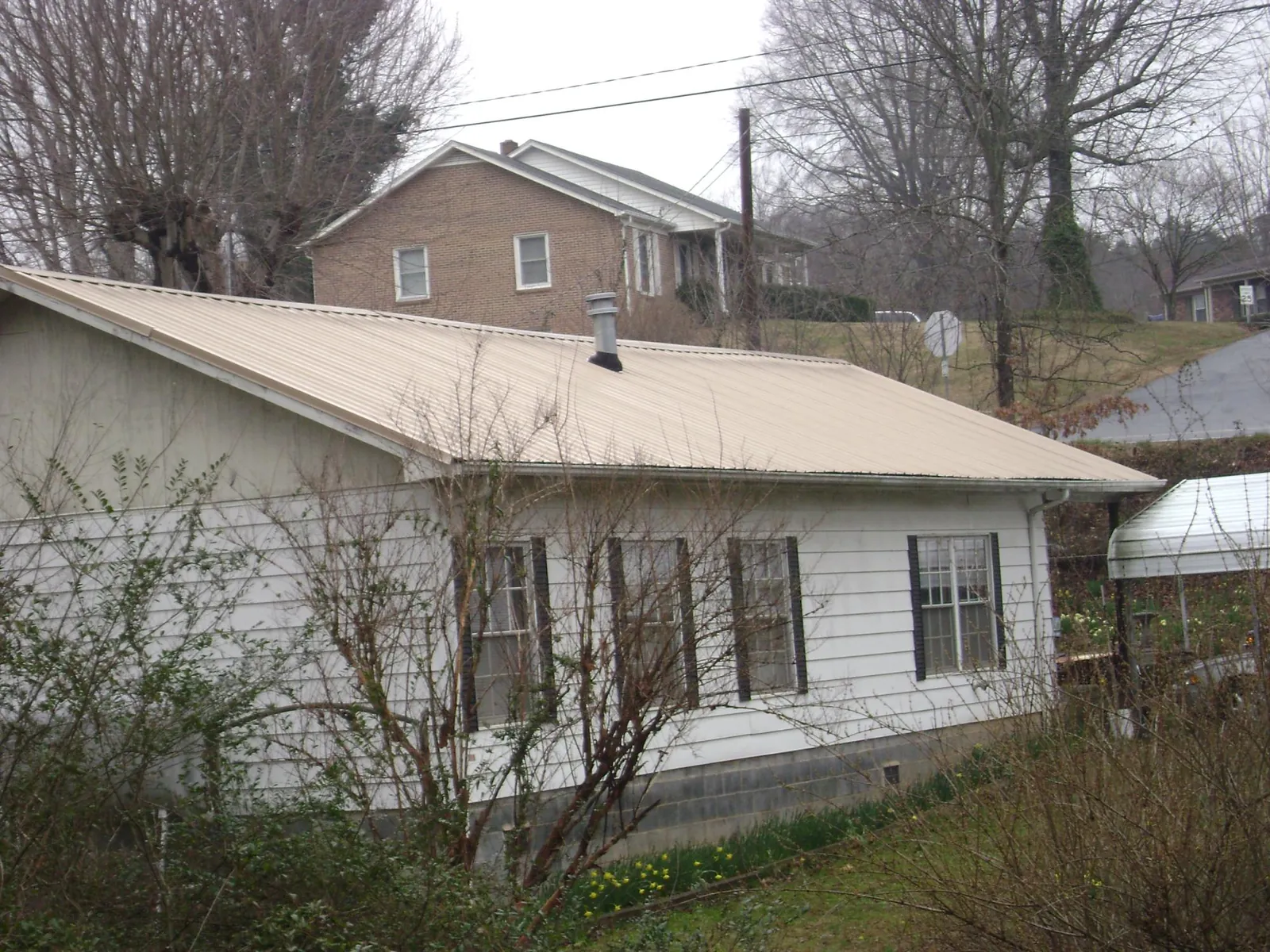 Tan metal roof on a white sided house set into a hillside — Commercial Roofing by Roofing Brothers in Wilbraham
